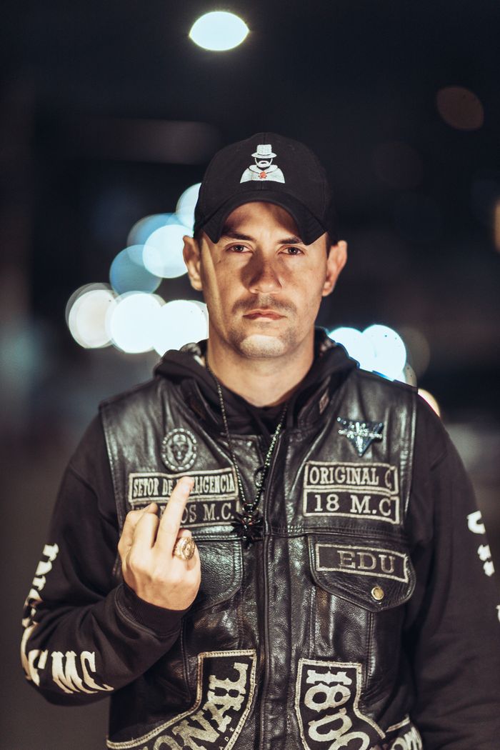 Mastering the First Impression: Your intriguing post title goes here A man at night wearing a leather jacket and hat, making a defiant hand gesture.