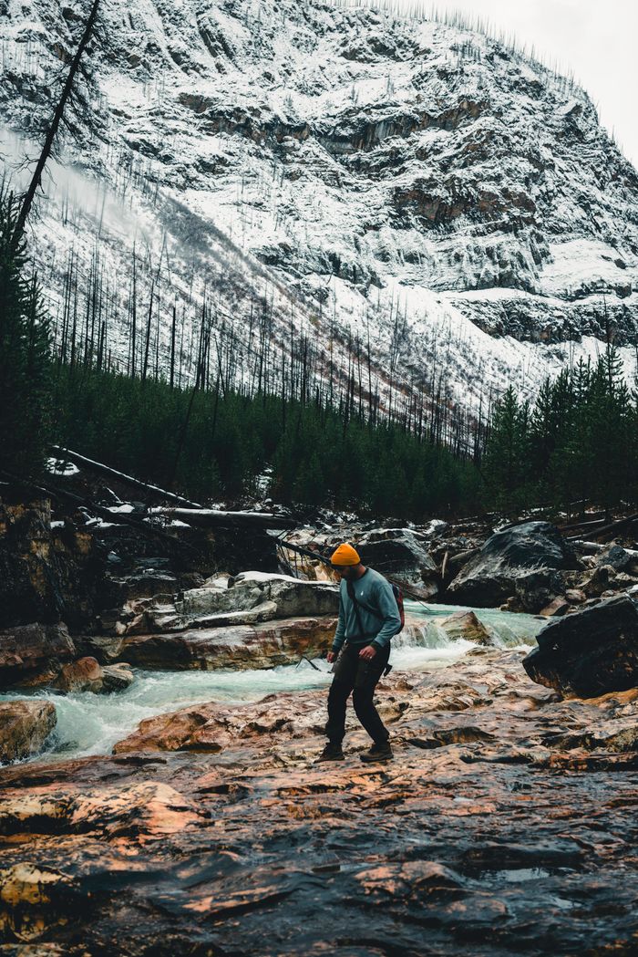 services-02 Man hiking through snowy wilderness in Kootenay Crossing, Canada, with rugged mountains and streams.