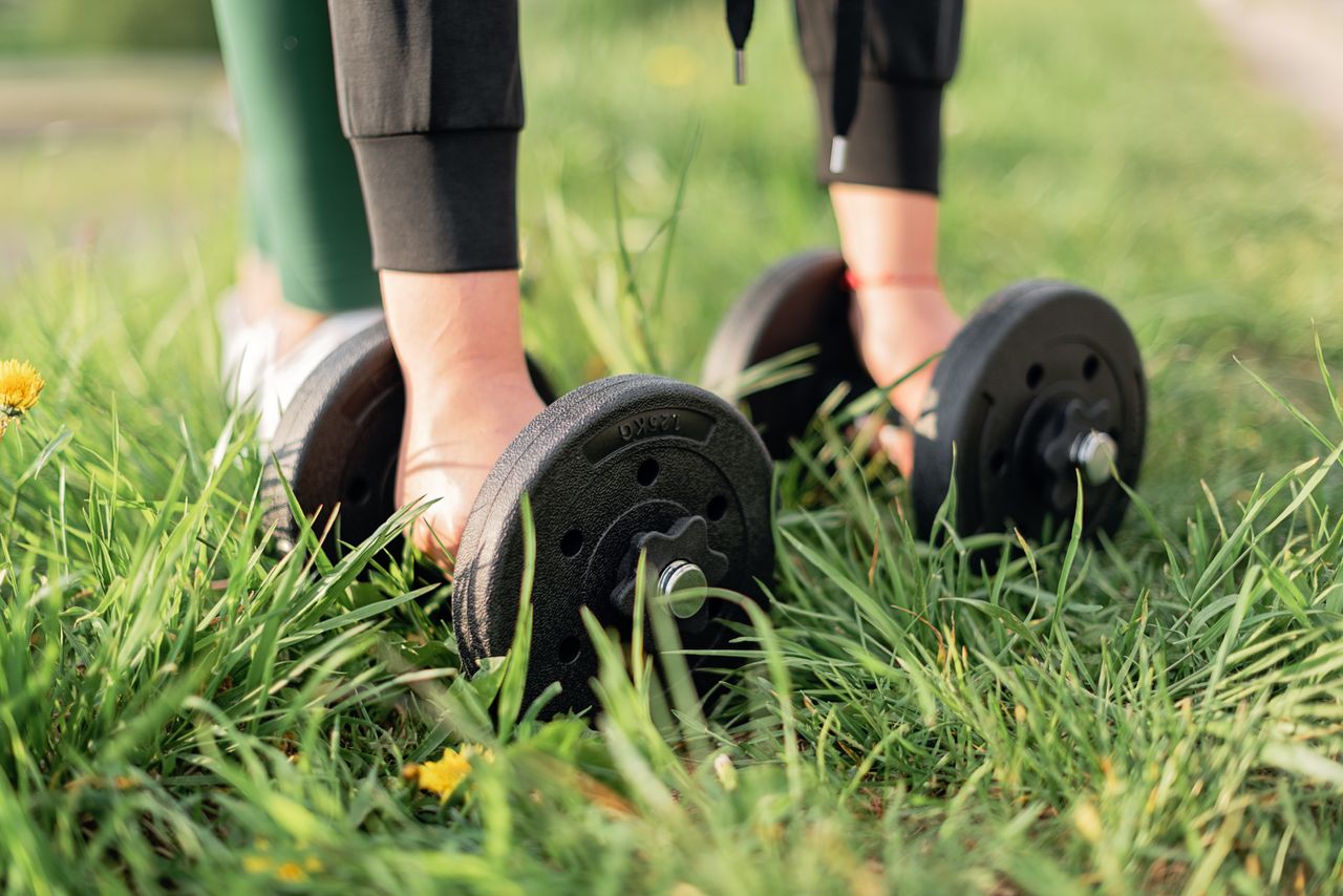 hero-img-01 Close-up of a person exercising outdoors with dumbbells on grass, emphasizing fitness and wellness.
