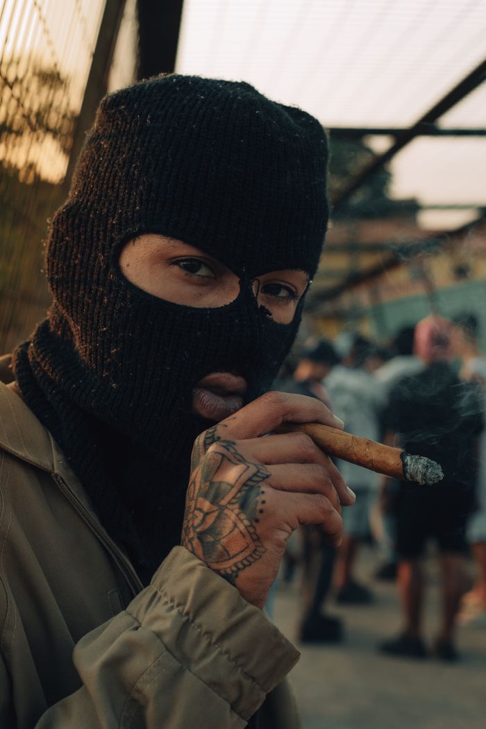 gallery-1 Close-up of a person wearing a balaclava and smoking a cigar outdoors, adding mystery and intrigue.